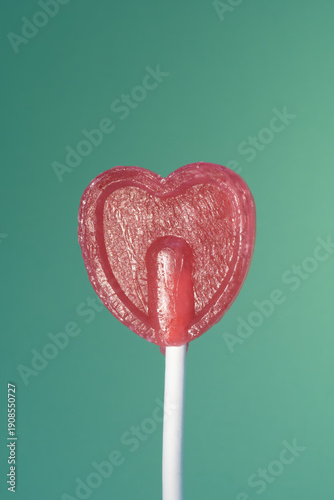 Redheart shaped lollipop on a stick against a green background, symbolizing love and sweetness