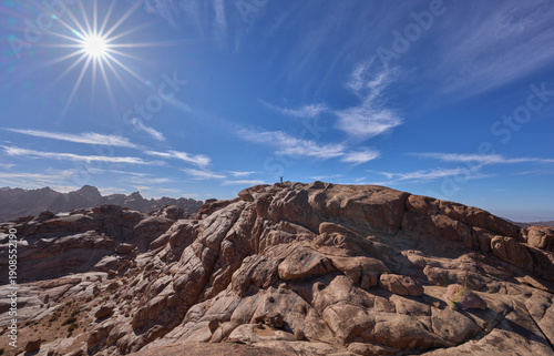 Mountain landscape with a female tourist posing in a summit in the national park Saint Catherine Protectorate, Sinai’s highlands. Red  granite mountains. Vacation in Egypt. Rays radiating from the sun
