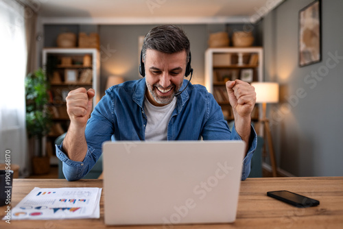 Bilde på lerret Excited man celebrating success during video call on laptop at home