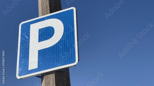 Blue parking sign on concrete pole against clear blue sky background with copy space
