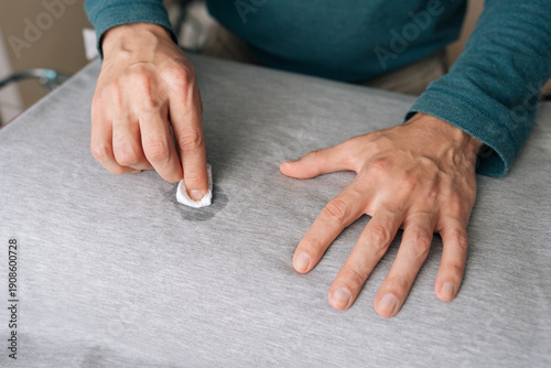 Canvas Print Person hands meticulously treating spill on gray fabric shirt using small white cloth soaked in cleaning agent, demonstrating household hygiene and laundry stain removal techniques