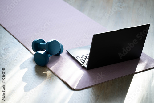 Laptop, dumbbells and resistance band on yoga mat at home. Online fitness training, home workout equipment, modern healthy lifestyle and digital fitness concept.
