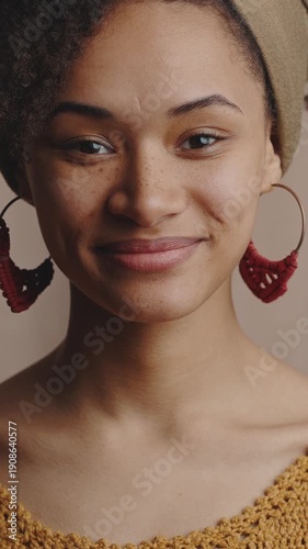 Close up portrait of young carefree stylish african american woman smiling to camera, beige studio background