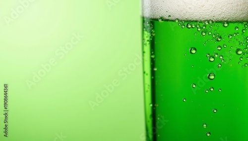 Green beer in glass with bubbles on green background  