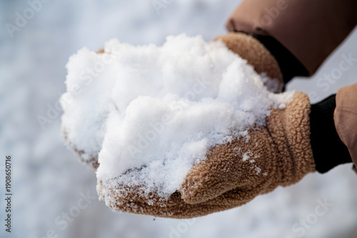 Person holding a pile of fluffy snowflakes in brown fleece gloves. Detail of fresh precipitation after a heavy snowfall or blizzard. Photo