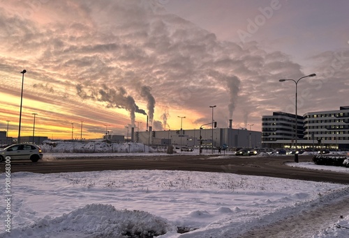 Dawn in the industrial part of the city, a factory with smoking chimneys, a road with heavy traffic, environmental pollution, winter season with snow