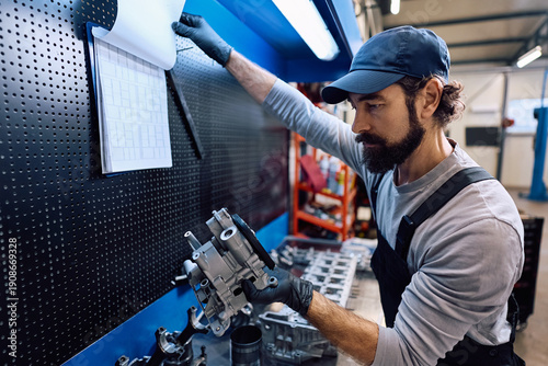 Картината върху платно Mature mechanic examining parts for vehicle technical servicing in workshop