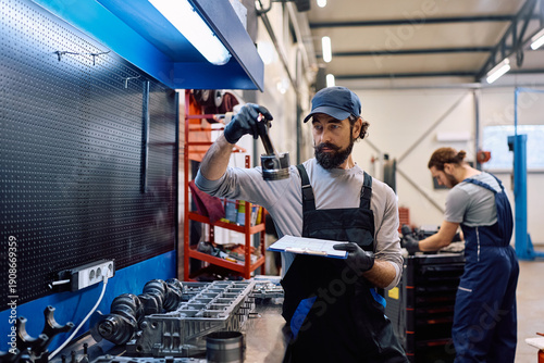 Quadro em tela Car mechanic examining vehicle parts on workbench while working in auto repair shop