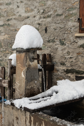 A rustic stone fountain runs beneath fresh snow, where clear water keeps flowing, capturing winter stillness, rural charm, and the quiet persistence of nature