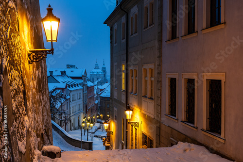 Winter morning with glowing gas lamps in snowy Prague - view of Lesser Town from the stairs in the historic center near Prague Castle