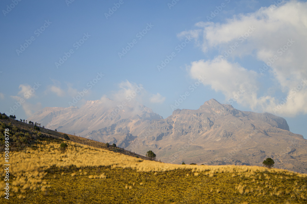 Fototapeta premium Natural highland landscape with dry meadow and mountain range under blue sky, suitable for backgrounds and environmental concepts.