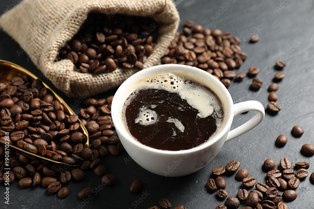 Fototapeta premium Aromatic coffee in cup and beans on black table, closeup
