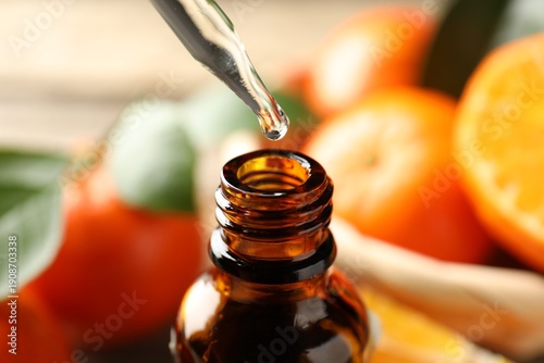Dripping tangerine essential oil into bottle on table, closeup