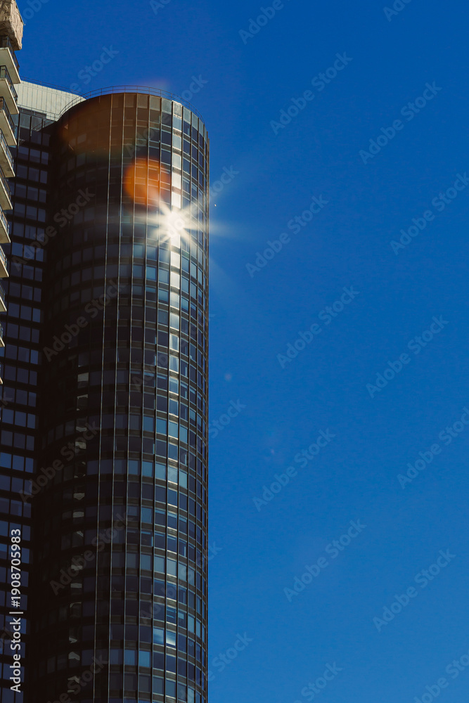 Obraz premium Sunlight reflects off a glass building in a city on a clear day with no clouds in the sky showcasing the urban landscape and architecture from a low angle view