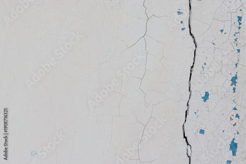 White peeling paint on the wall. Old concrete wall with cracked flaking paint. Weathered rough painted surface with patterns of cracks and peeling. High resolution texture for background and design.