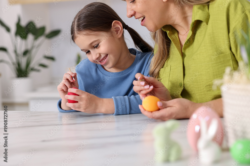 Fototapeta premium Easter celebration. Mother and her daughter painting eggs at white marble table in kitchen, closeup