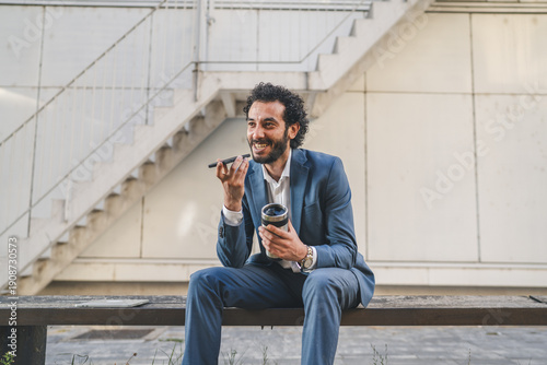 Bild auf Leinwand Businessman talking on speakerphone and drinking coffee outdoors