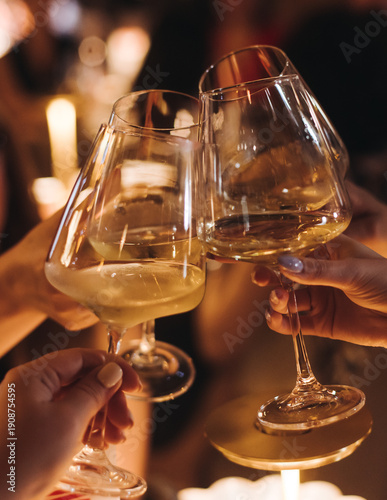 Group of guests celebrate and raise glasses, toasting and cheering with alcohol glasses with wine and champagne in the restaurant on corporate christmas birthday party event or wedding celebration