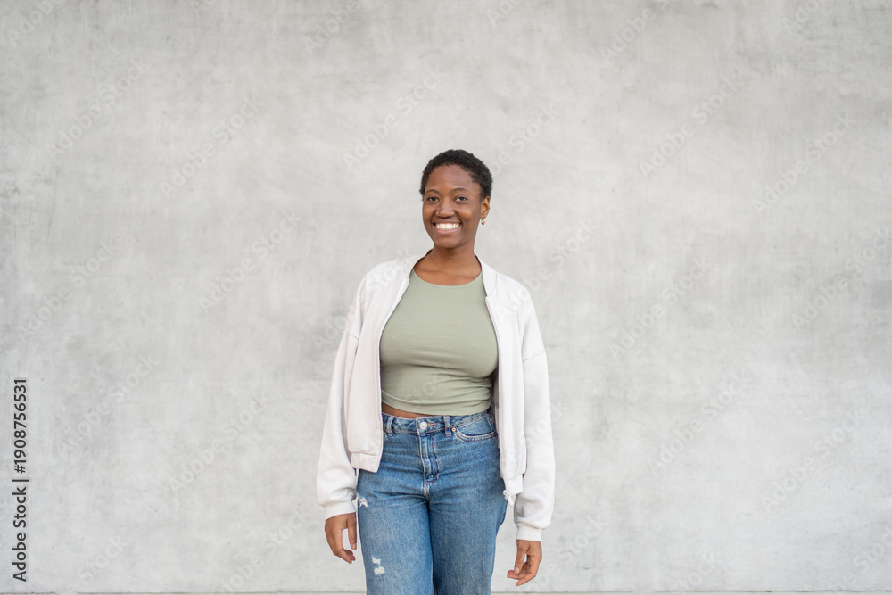 © Andrii - Smiling young black woman standing against gray wall wearing trendy casual clothes. Friendly expression with relaxed mood and modern everyday style © Andrii - Smiling young black woman standing against gray wall wearing trendy casual clothes. Friendly expression with relaxed mood and modern everyday style