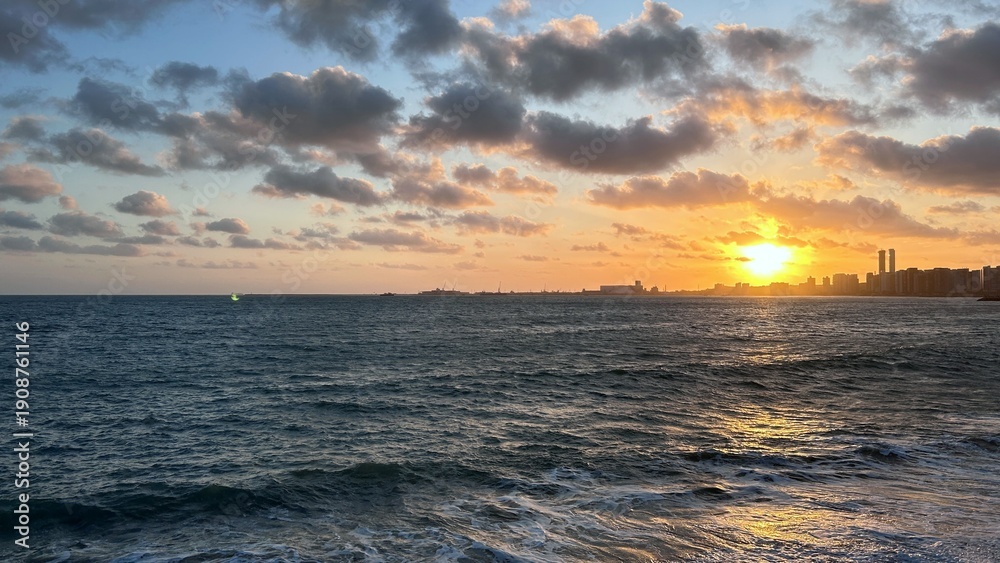 Obraz premium Golden Sunset Over Ocean Waves with Coastal City Skyline
