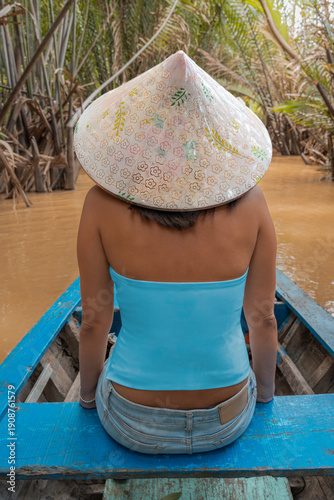 Tourist wearing a conical hat enjoying a boat ride on the Mekong Delta in Vietnam