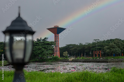Beautiful rainbow arching over a water tower and lotus pond in a serene park
