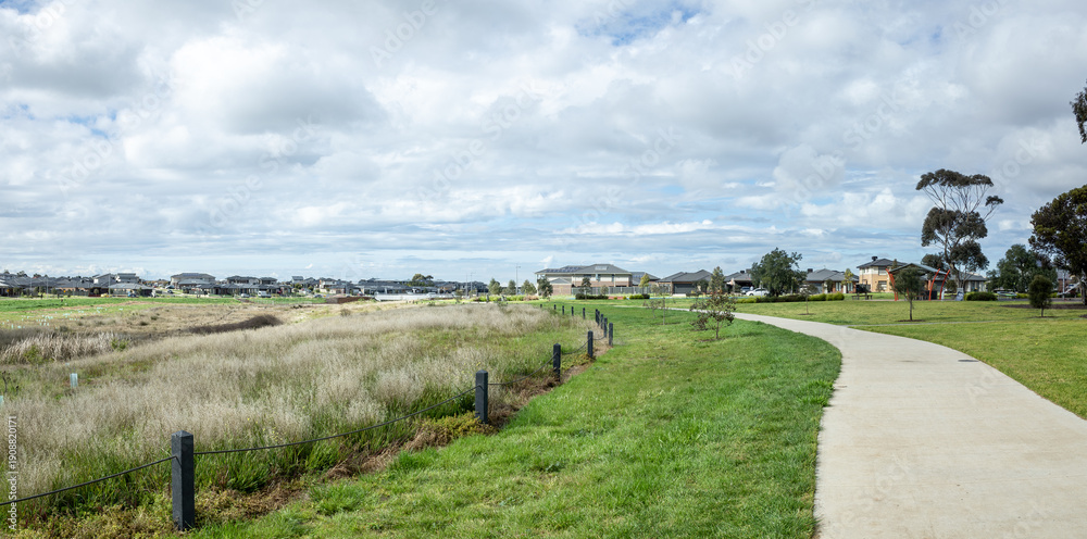 Fototapeta premium A curved pedestrian path running alongside a natural wetland area in a modern suburban residential development in Australia. Urban green infrastructure, environmental planning, and outdoor parkland