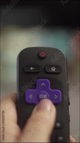 Woman's hand pressing the ok button on a smart tv remote control to select a program on a streaming media player
