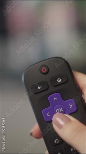 Close-up of a female hand holding a roku remote, navigating through options and pressing the ok button to watch a movie or tv show