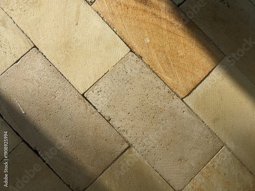 Top view of rectangular limestone pavers in warm earth tones. The surface features a natural porous texture with a sharp diagonal shadow cast across the stone blocks.