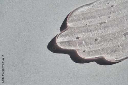 Clear skincare serum gel smear on gray background, showcasing texture and air bubbles