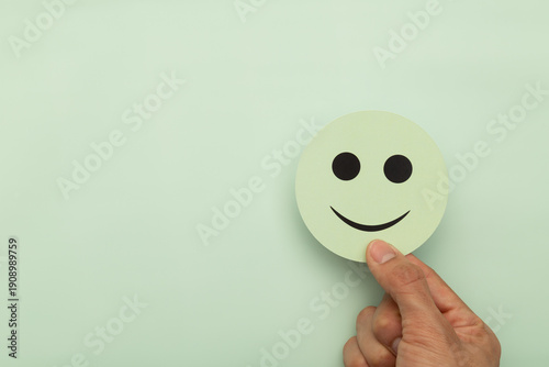 Fotografia Hand holding a green smiley face over a pastel background