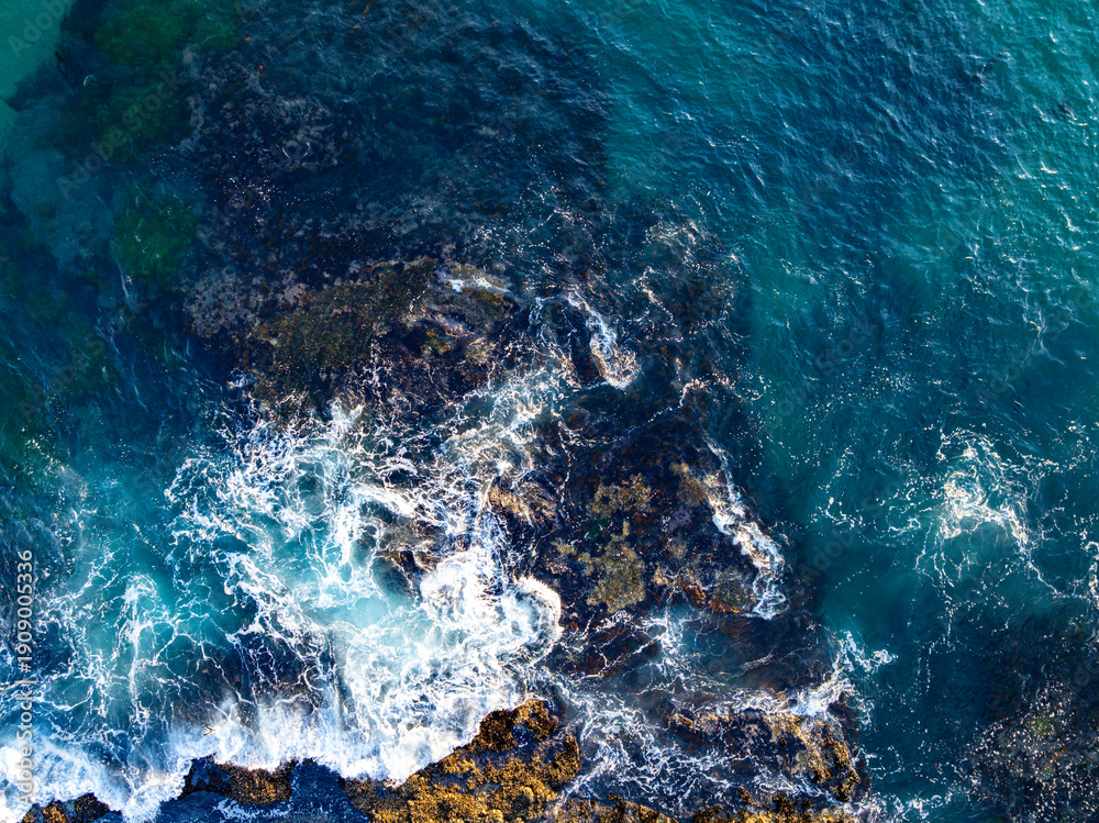 Obraz premium Turquoise water with reef. Blue ocean water. Coastline from above. Summer beach with crashing waves. Dramatic coastline. Ocean surface. Rocky coast with sea foam. Wave moving.