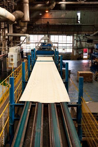 A plywood manufacturing facility showcases machinery processing sheets of plywood. Workers oversee operations in the large, well-equipped industrial space.