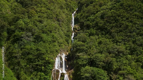 Dynamic aerial parallax shot revealing Cascadas Chamana waterfall hidden within dense tropical forest on mountain slope under soft light in Banos Ecuador
