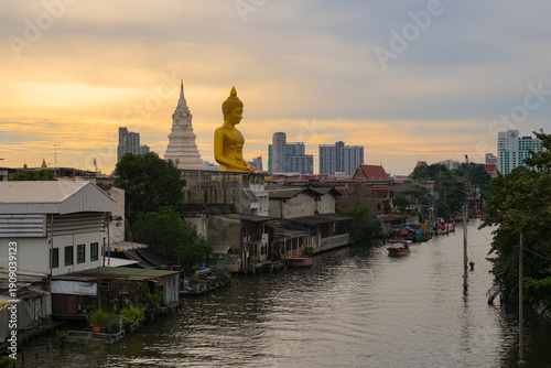 Wat Paknam Phasi Charoen, Thailand, majestic Big Buddha rising above the Bangkok skyline at sunset. Long-tail boat moves along canal.
Big Buddha of Wat Paknam Phasi Charoen stands as a  landmark.