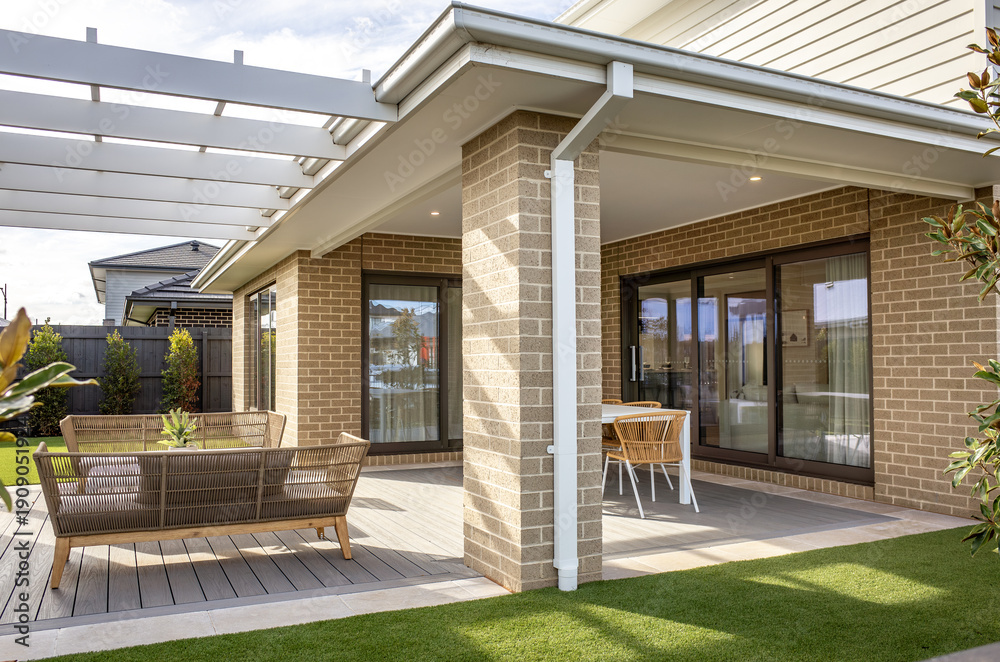 Ταπετσαρία A covered outdoor patio with timber decking and contemporary outdoor furniture attached to a house, overlooking backyard garden
