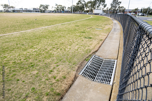 Tableau sur toile A stormwater drainage grate installed along the edge of a fenced sports field in a suburban park in Australia