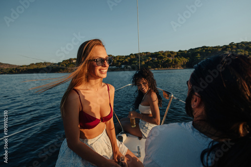 Fotografi Friends enjoy a sunny sailing trip aboard a boat on calm blue waters