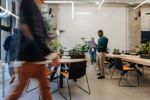 African American man with laptop in a modern Madrid coworking space as coworkers move around