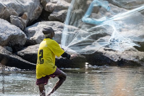 A Thai fisherman with a net catches fish in the coastal area on a sunny morning