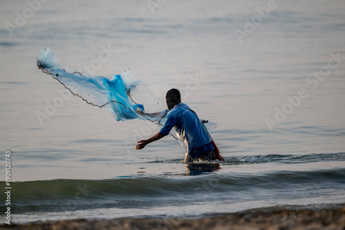 Obraz na plátne A Thai fisherman with a net catches fish in the coastal area on a sunny morning