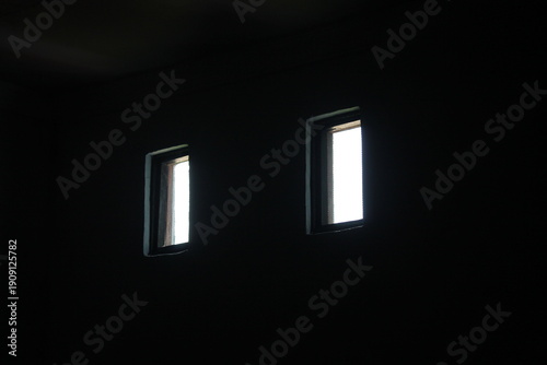 Two bright windows in a dark room creating a minimalist silhouette effect. Concept of hope, light at the end of the tunnel, and architectural art.
