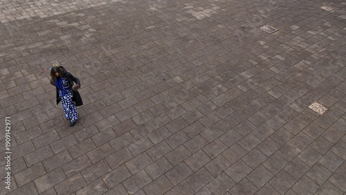 Overhead view of a woman in a patterned dress walking on a paved plaza