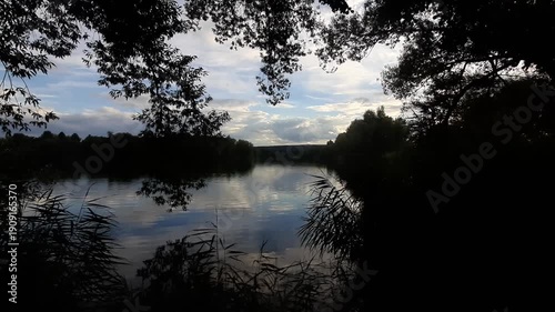 Cloudy day lakeshore landscape framed between trees with vegetation silhouette near Regensburg Germany