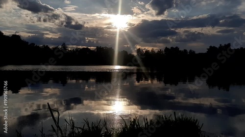 Golden sun sets behind forest silhouettes reflecting in calm lake water at dusk near Regensburg
