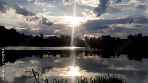 Golden sun sets behind forest silhouettes reflecting in calm lake water at dusk near Regensburg