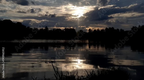 Golden sun sets behind forest silhouettes reflecting in calm lake water at dusk near Regensburg