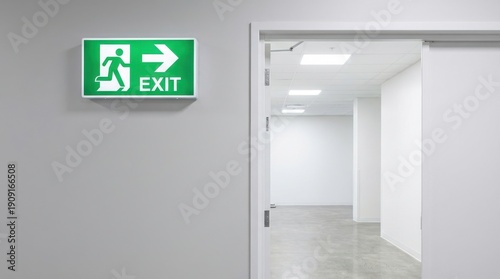Green exit sign with person running and arrow on a white wall above open door