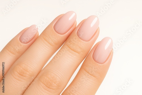 Close-up of a woman's hand with elegant oval-shaped nails, painted with a delicate nude pink polish, showcasing clean, modern nail art on a neutral background.